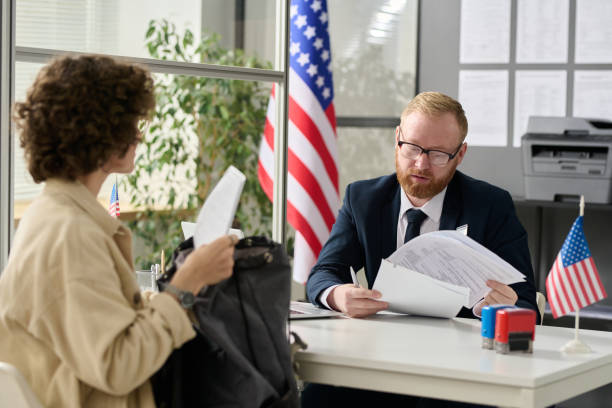 Young woman applying for visa in US immigration office Portrait of male worker revising documents of young woman applying for visa in US immigration office Bureaucracy stock pictures, royalty-free photos & images