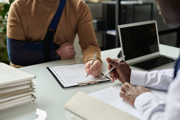 Close up of man filling in medical insurance form Close up of man filling in medical insurance form, injured hand in sling in background, copy space injured stock pictures, royalty-free photos & images