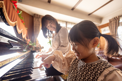 Little girl playing the piano with her mother at home