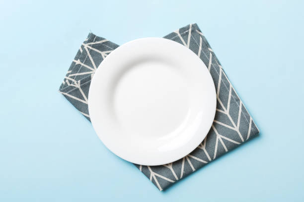 istock Top view on colored background empty round white plate on tablecloth for food. Empty dish on napkin with space for your design 1452137168