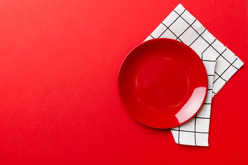 Top view on colored background empty round red plate on tablecloth for food. Empty dish on napkin with space for your design.