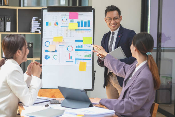 istock Team business three smiling and happy Asian men and women team using tablets and laptops brainstorm and plot statistics on a corporate chart board inside the company. Colleagues concept. 1452137421