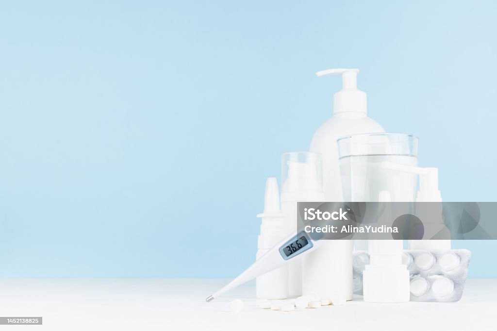 Medical and treatment background with white bottles mockup for prevent and teraphy disease and sickness, health - 36,6 thermometer, sprays, salves, pills on white table, blue wall, copy space. Advertisement Stock Photo