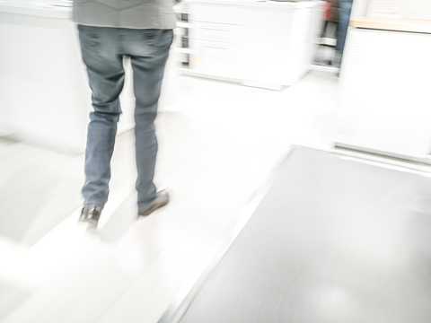Legs and feet of a person seen from behind walking around in a shop - motion blur, high key