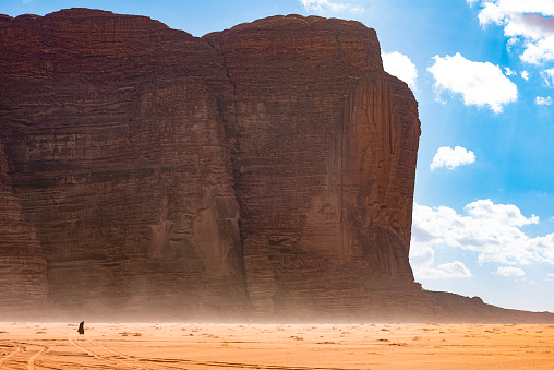 The Wadi Rum desert is one of the most picturesque and beautiful touristic spots of Jordan. In the picture a lone man walking in the dust in front of a mountain ridge in the desert on a beautiful winter afternoon.