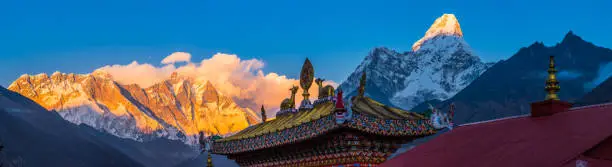 Mt. Everest, Nuptse, Lhotse and Ama Dablam illuminated by sunset light overlooking the golden rooftop of Tenboche Monastery high in the Himalayan mountains of Nepal.