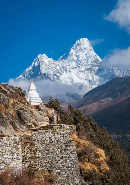 Poerter carrying heavy load around a traditional Buddhist stupa on the Everest Base Camp trail beneath the iconic snowy spire of Ama Dablam (6812m) high in the Himalaya mountain wilderness of the Sagarmatha National Park, a UNESCO World Heritage Site in Nepal.