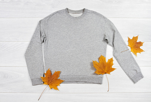 Close up gray blank template sweatshirt hoodie with copy space. Autumn concept yellow leaf. Top view mockup pullover on white wooden background. Casual outfit. Flat lay template clothes.