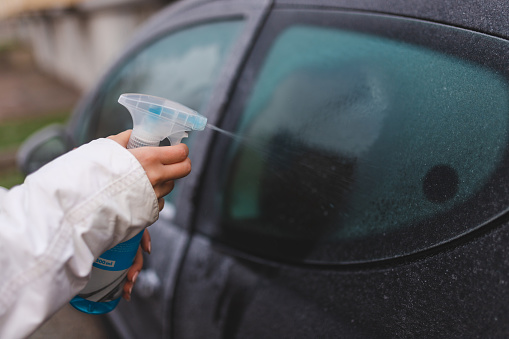 Close-up of a young woman spraying a defrosting solution on her car window.