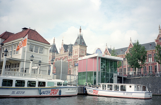 Amsterdam, Netherlands - 1984: A vintage 1980's Nikon negative film scan of the city of Amsterdam across the Amstel river canal with houseboats docked.