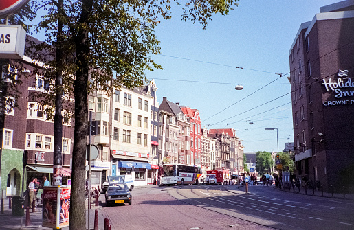 Amsterdam, Netherlands - 1984: A vintage 1980's Nikon negative film scan of streets and buildings in central Amsterdam with cars and pedestrians traveling.