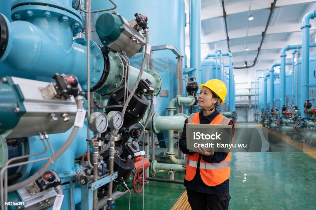 A female engineer works in a chemical plant using a laptop computer Industry Stock Photo