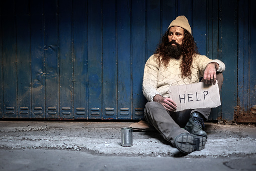 A young woman giving money to homeless beggar man sitting outdoors in city.