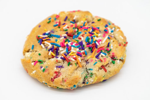 A closeup of a simple sugar cookie topped with colorful sprinkles on a white background
