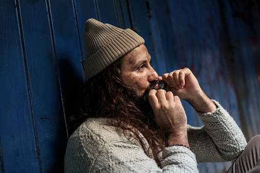 Homeless man playing a harmonica on the street. About 45 years old, Caucasian male.