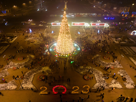 Bishkek, Kyrgyzstan - December 24, 2022: Aerial view of Christmas tree with Coca-Cola trucks on a square with people