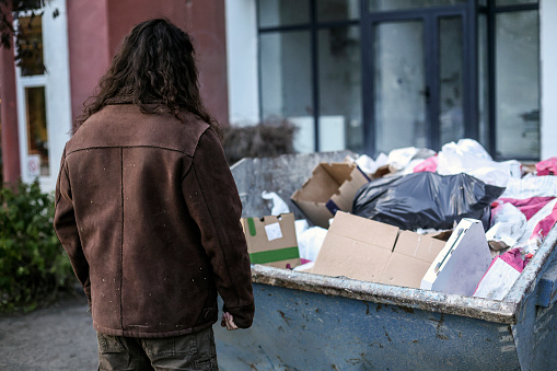 Homeless man on the street searching through a dumpster. About 45 years old, Caucasian male.