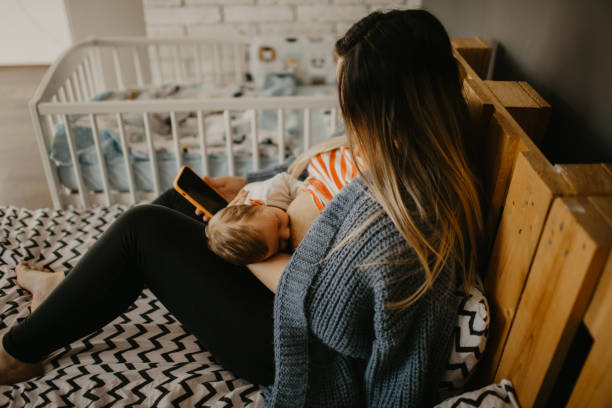istock High-angle view of a mother breastfeeding her baby boy while sitting on the bed and using a phone 1452172946