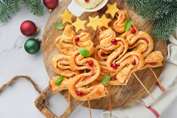 istock Christmas or New Year appetizer. Christmas tree shape puff pastry buns with cheese and ham. Group of Christmas tree shapes on wooden board. Festive idea for Christmas or New Year dinner. Top view. 1452173326