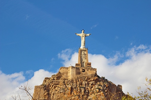 The statue of Jesus and the castle of Castillo de Monteagudo in Spain against the blue sky