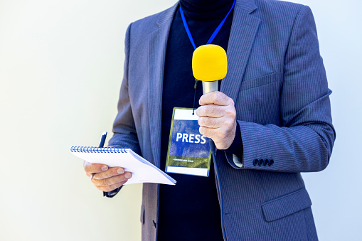 TV reporter at news event, press conference or journalistic media interview holding yellow microphone. Broadcast journalism concept with copy space.