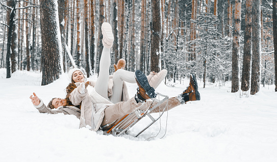 Love romantic young couple girl,guy in snowy winter forest with christmas tree, sled.Walking with sleigh in stylish clothes, fur coat,jacket, woolen shawl, bonnet.Snow lovestory.Romantic date,weekend.