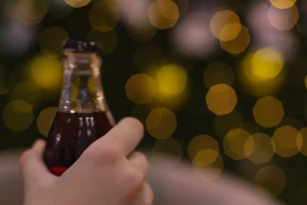 Photo of Girl's hand in blur holds bottle of Coca-Cola soft drink on bokeh background.Christmas mood.New year