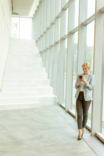 istock Businesswoman using mobile phone on modern office hallway 1452196641
