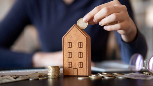 Hand putting coin in house model of coin for saving money for buying house. stock photo