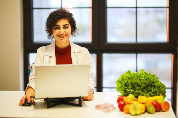 istock Smiling brunette female nutritionist in her office writing diet plan showing healthy vegetables and fruits. Health and diet concept. Life style. 1452215849
