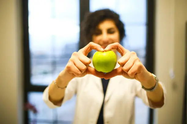 Photo of healthy nutritionist holding apple in heart shape in his office. healthy eating concept. lost weight