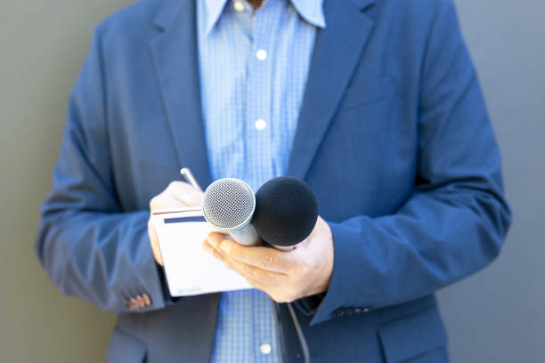 istock Journalist at media event or news conference, holding microphone, writing notes. Broadcast journalism concept. 1452224009