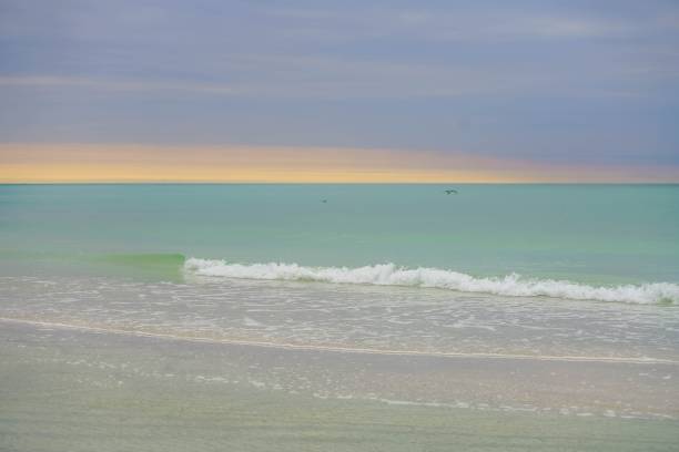 Sun setting behind clouds over turquoise water and white sand at Anna Maria Island in Florida stock photo