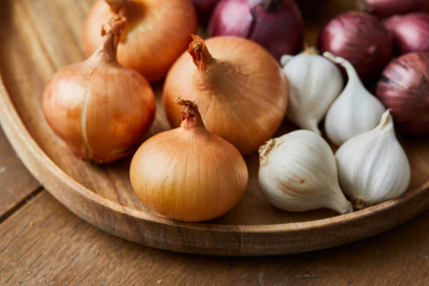 Garlic, onion and Spanish red onion on a wooden plate Garlic, onion and Spanish onion on a wooden plate, seasoning vegetables on a wooden kitchen table top, a top view with a copy space area onion family stock pictures, royalty-free photos & images