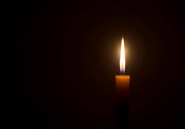 istock A single burning candle flame or light glowing on an orange candle on black or dark background on table in church for Christmas, funeral or memorial service with copy space 1452242407