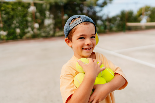 Photo of a little boy at the tennis court holding tennis balls