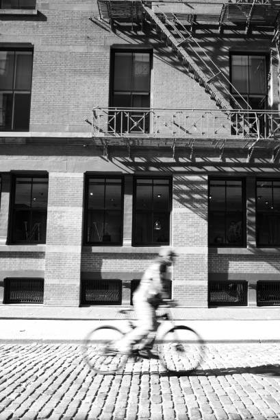 Man riding a bicycle in the street on a sunny day\nNew York\nBlack and white