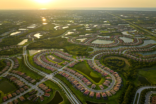 Aerial view of tightly packed homes in Florida closed living clubs with lake water in the middle. Family houses as example of real estate development in american suburbs.