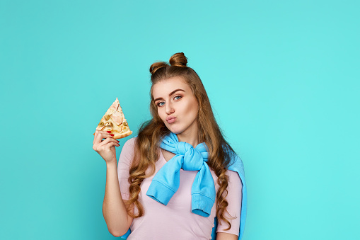 funny girl with pizza slice on blue background. copy space