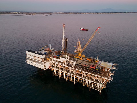 Drone Shot Massive Off-Shore Drilling Rig, Used for Drilling and Fracking for Crude Oil and Natural Gas, with Long Beach and Los Angeles California in the Background at Dusk