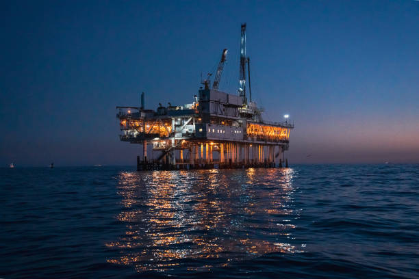 operazioni notturne di perforazione e fracking di piattaforme petrolifere offshore, illuminate a colori vivaci, in mare calmo - oil rig oil sea mining foto e immagini stock