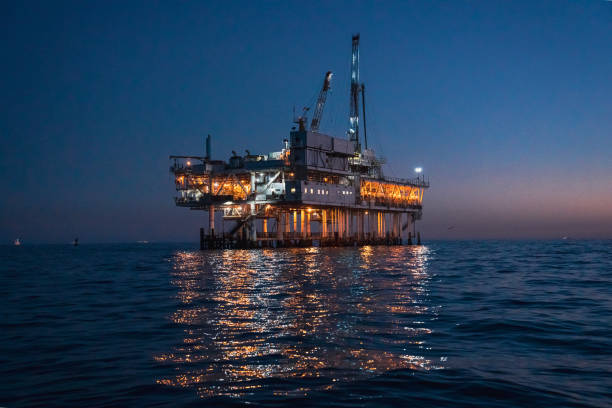 nocne wiercenie i szczelinowanie na morskich platformach wiertniczych, jasno oświetlone, na spokojnym morzu - oil pump sunset mining drilling rig zdjęcia i obrazy z banku zdjęć
