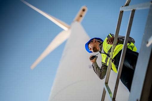 Asian engineers working in fieldwork outdoor. Workers check and inspect construction and machine around building project site. Wind turbine for electrical of clean energy and environment sustainable.