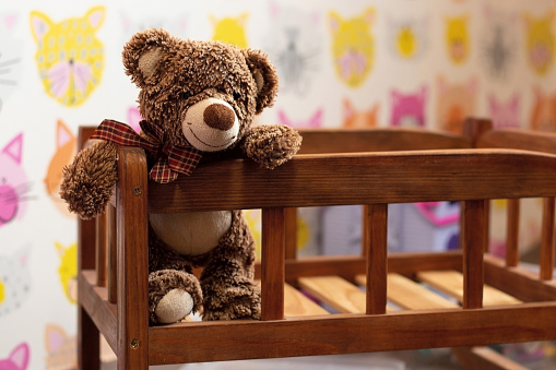 soft brown teddy bear sits in a children's wooden bed in a children's room on a blurred background