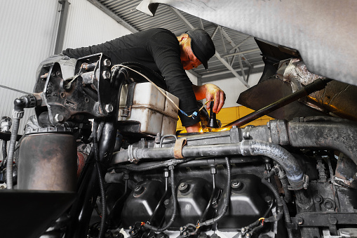 Car mechanic repairs large truck or tractor in workshop. Professional mechanic repairs truck engine. Genuine worker..