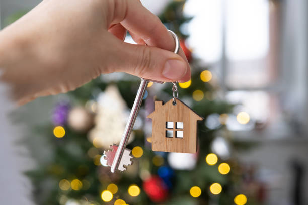 Key to the house in hand on background of Christmas tree. Gift for New Year, Christmas. Building, design, project, moving to new house, mortgage, rent and purchase real estate. Copy space stock photo