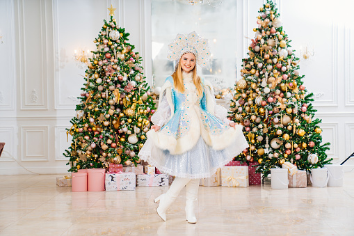 Snow Maiden in a traditional costume with short skirt and a kokoshnik in a room with christmas tree. The concept of Russian New Year's traditions. Congratulations to children.