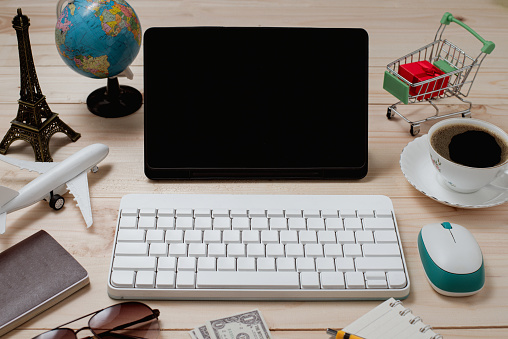 Travel and business concept with keyboard accessories and passport on rustic wooden table background. Vacation Globe, cup, cart, airplane, compass, and tablet blank screen for text. Top view