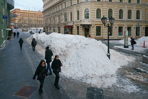 Moscow, Russia - February 19, 2021:  People go on the city street in the cold winter day. Cleaned town after snowy blizzard. Lifestyle concept. Famous Lubyanka Building in distance. High angle view