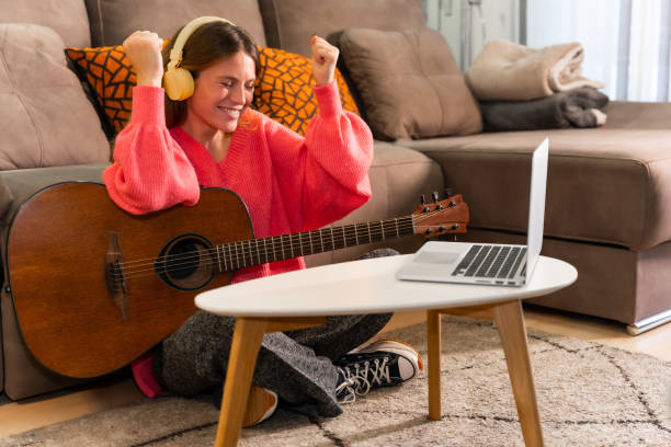 istock Woman learning to play the guitar at home with online classes on the computer, smiling because she has played the song well 1452307330